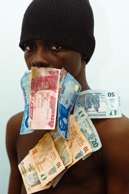 This image shows a person wearing a black knit beanie, with a serious expression, holding a variety of British pound banknotes—£20, £50, and £10 notes—close to their face and draped around thei